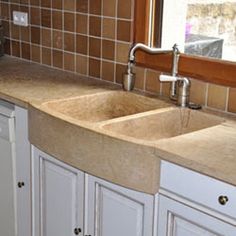 a kitchen sink with two faucets in the middle and brown tiles on the back