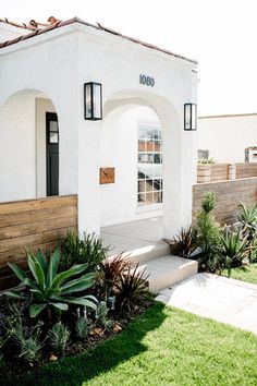 a white house with plants in front of it and a wooden fence around the entrance