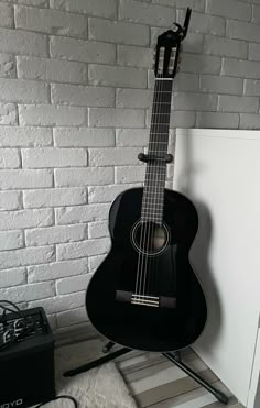 a black acoustic guitar sitting on top of a white floor next to a brick wall