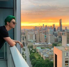 a man with green hair standing on top of a building looking out at the city