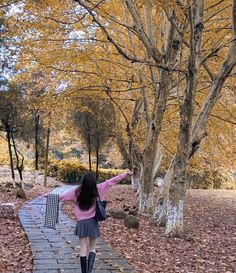 a woman walking down a path with her arms outstretched in front of trees and leaves on the ground