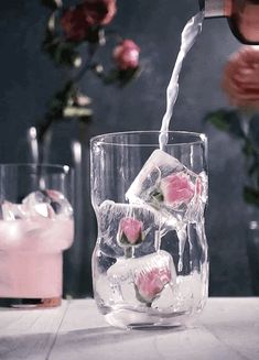 a person pouring water into a glass filled with ice and pink flowers on the table