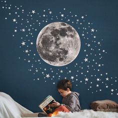 a young boy reading a book in front of a full moon and stars wall decal