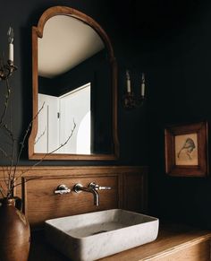 a bathroom sink sitting under a mirror next to a vase with flowers on top of it