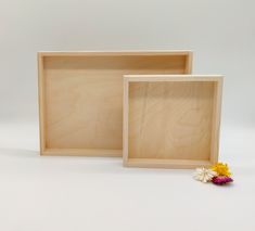 two empty wooden trays sitting next to each other on a white surface with a flower in the middle