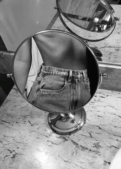 the reflection of someone's jeans in a round mirror on a marble counter top