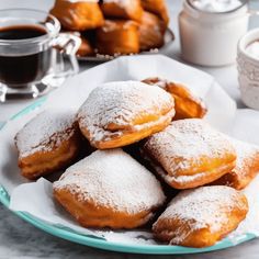 powdered sugar covered donuts on a plate next to cups of coffee and tea