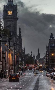 a city street filled with lots of traffic under a cloudy sky and clock tower in the distance