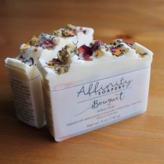 two soap bars sitting on top of a wooden table next to each other with different types of flowers in them