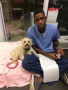 a man in scrubs sitting on a hospital bed with a small dog next to him