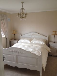 a white bed sitting in a bedroom next to a window and a chandelier