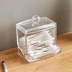 a glass container with toothbrushes in it sitting on a table next to a pen