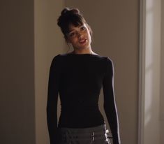 a woman in black shirt and grey skirt posing for the camera with her hands on her hips