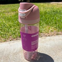 a pink water bottle sitting on top of a cement slab in front of green grass