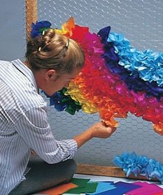 a woman sitting on the ground holding up a colorful piece of art made out of paper