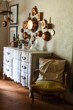 a room with many pots and pans hanging on the wall above a white dresser