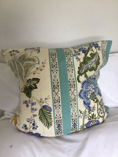 a white bed topped with a pillow covered in blue and green floral designs on it