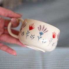 a hand holding a white cup with red and blue flowers on it's rim