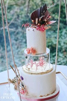 a three tiered cake with flowers and feathers on top