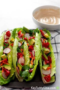 raw vegan rainbow tacos with thai lime dressing on a tray next to a bowl of dipping sauce