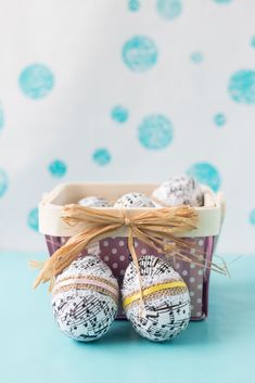 three decorated easter eggs in a basket on a blue surface with polka dots and twine