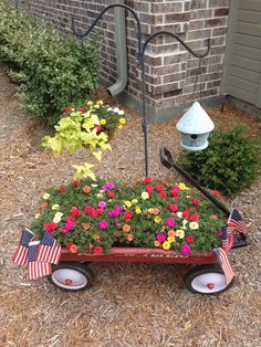 a wagon filled with flowers sitting in front of a brick building next to a flag pole