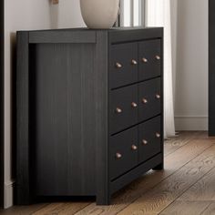 an empty vase on top of a black dresser in a room with wood flooring