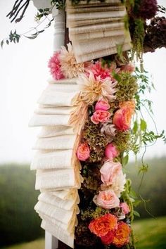 an arrangement of books and flowers hanging from a wooden pole in front of a field