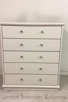 a white dresser with six drawers and chrome knobs on the bottom, next to a wall