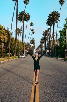 a woman is skateboarding down an empty street with palm trees in the back ground