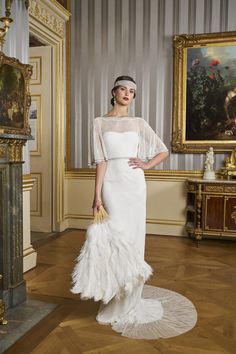 a woman in a white dress and feathered hat standing on a wooden floor next to a painting