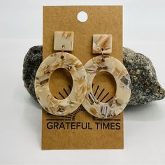 a pair of wooden earrings sitting on top of a rock next to a card board