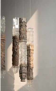 three glass vases hanging from the ceiling in front of a wall with light coming through them