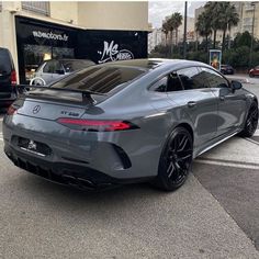 the rear end of a grey sports car parked in front of a building on a city street