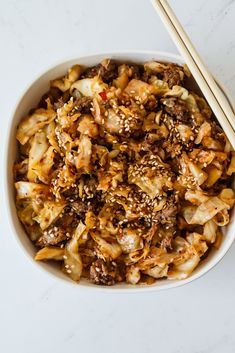 a bowl filled with noodles and meat next to chopsticks on a white surface