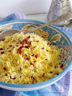 a bowl filled with yellow rice on top of a blue and white towel next to a spoon