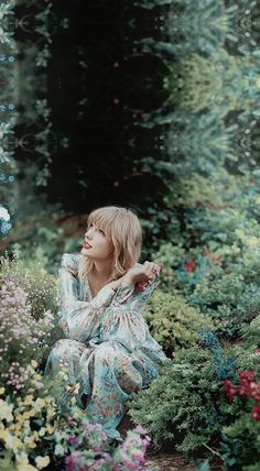 a woman sitting on the ground in front of some flowers and plants with her eyes closed