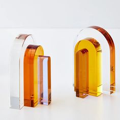 two orange and clear glass objects sitting on a white surface, one is shaped like an arch