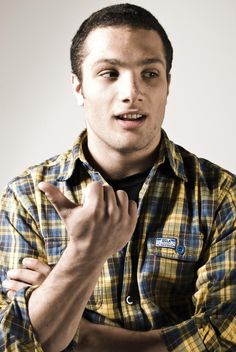 a man in a yellow and blue plaid shirt is holding his hand up to the camera