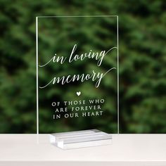 a clear acrylic sign with the words in loving memory on it and a forest background