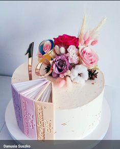 a cake decorated with flowers and books on top of a white table topped with an open book