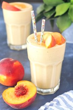 two glasses with peaches and strawberries in them on a blue table cloth next to some fruit