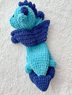 a crocheted stuffed animal laying on top of a white blanket covered in blue and green yarn