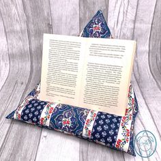 an open book sitting on top of a blue and white pillow with a floral pattern