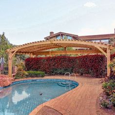 an outdoor swimming pool surrounded by shrubbery and a wooden pergolated cover over it