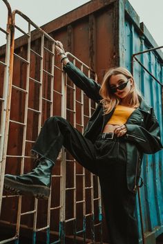 a woman in black pants and yellow shirt leaning against a metal fence