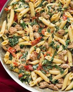 pasta with meat and spinach in a pan on a red cloth next to a wooden spoon