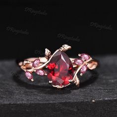 a red stone ring with leaves on the side and pink stones in the middle, sitting on top of a black surface