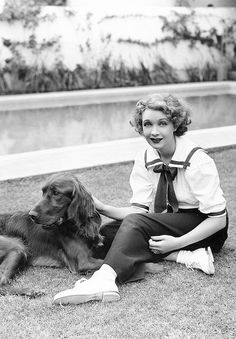 a woman sitting on the ground next to a brown dog and wearing a tie with her legs crossed