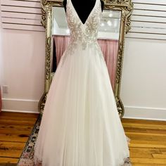 a white wedding dress is on display in front of a mirror with a gold frame